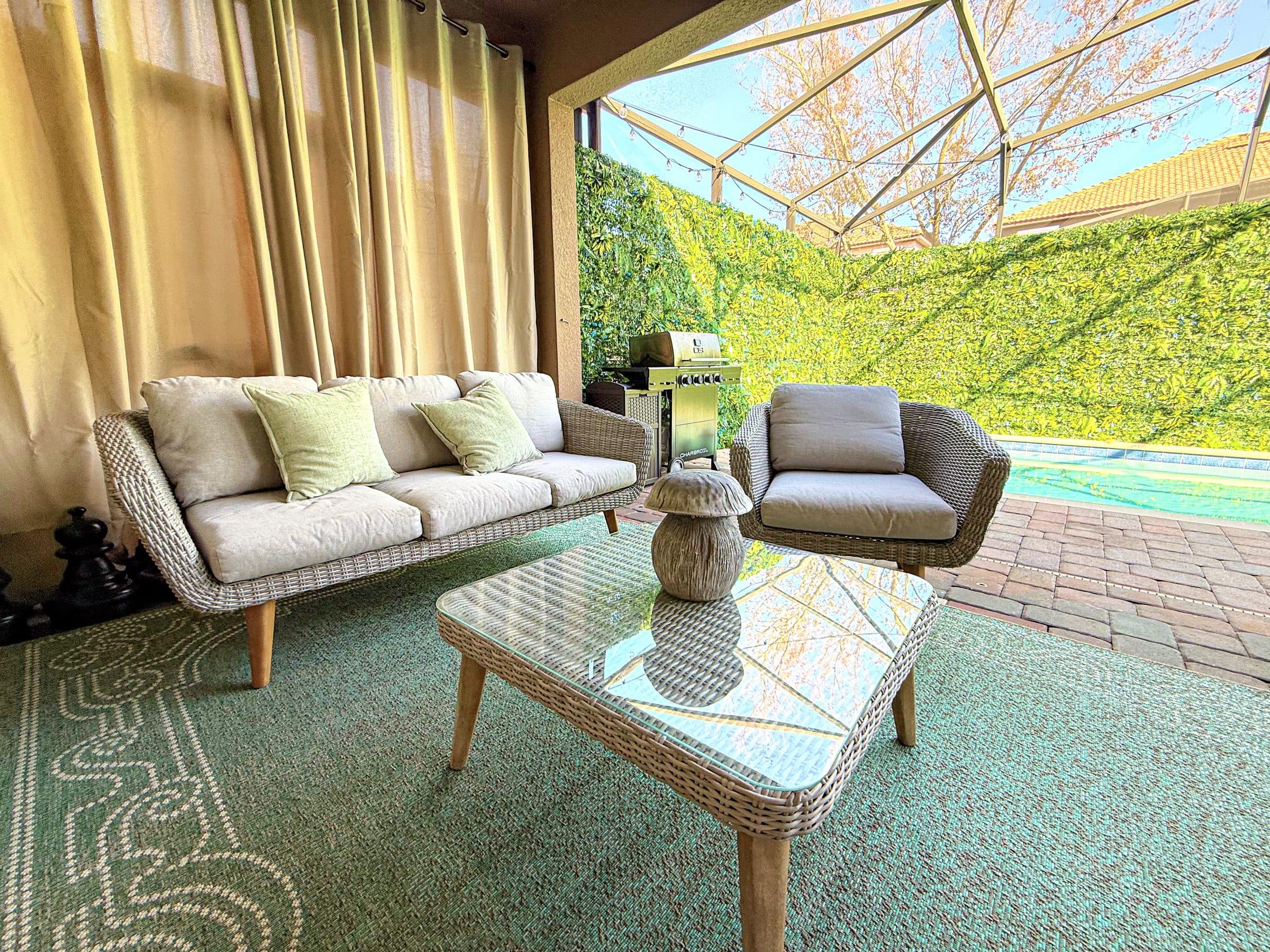Wicker sofa and armchair under the covered lanai, pool shimmering beyond. Seat y