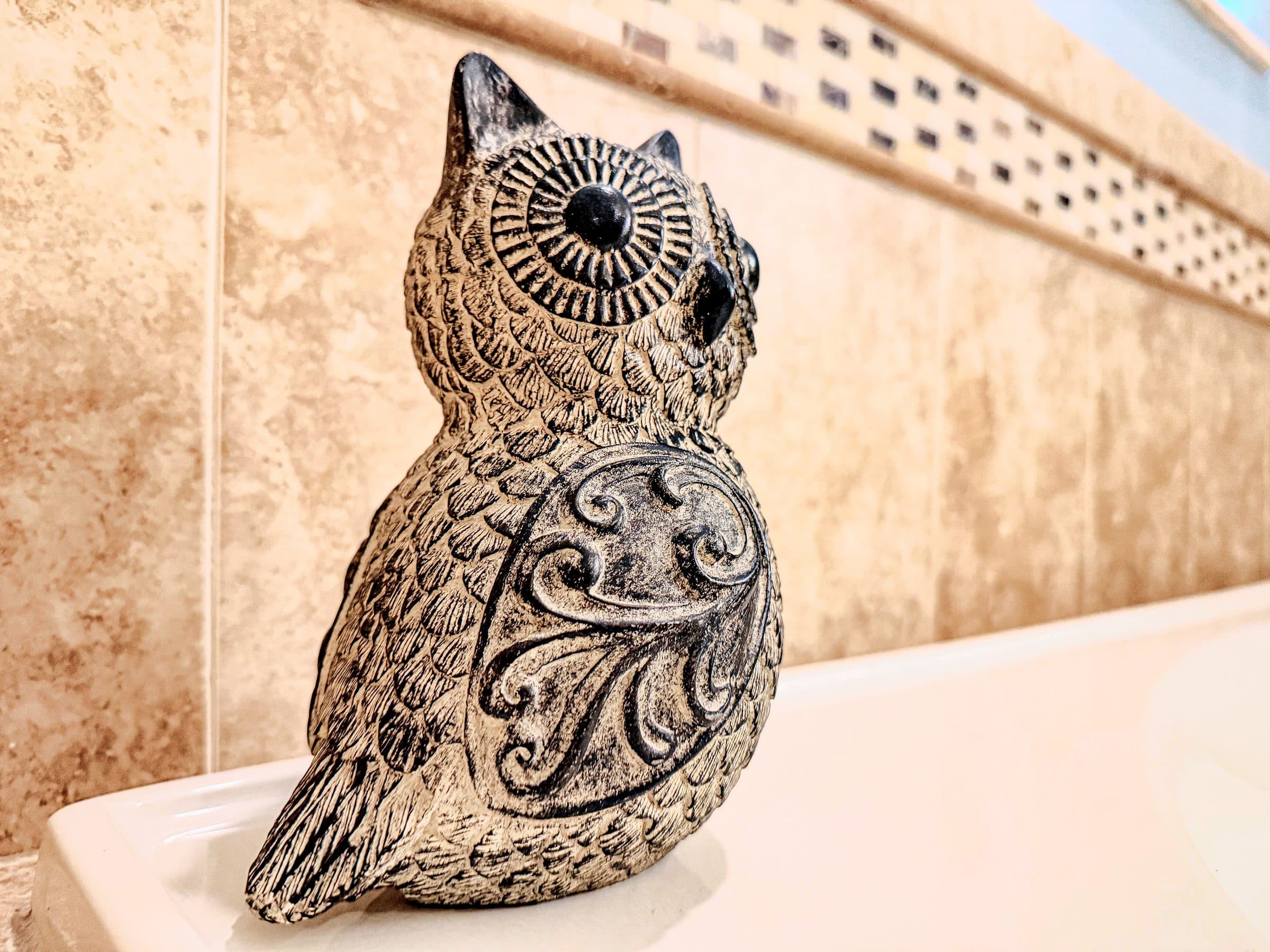Stone owl perched on the edge of the soaking tub, warm tile rising behind it. Ev