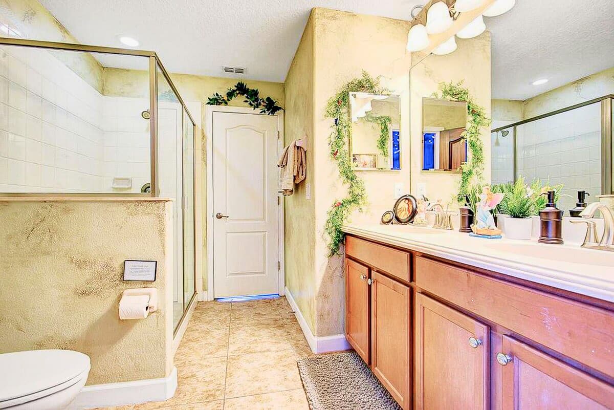 Ivy trailing across the mirror, a walk-in glass shower, and warm parchment-toned