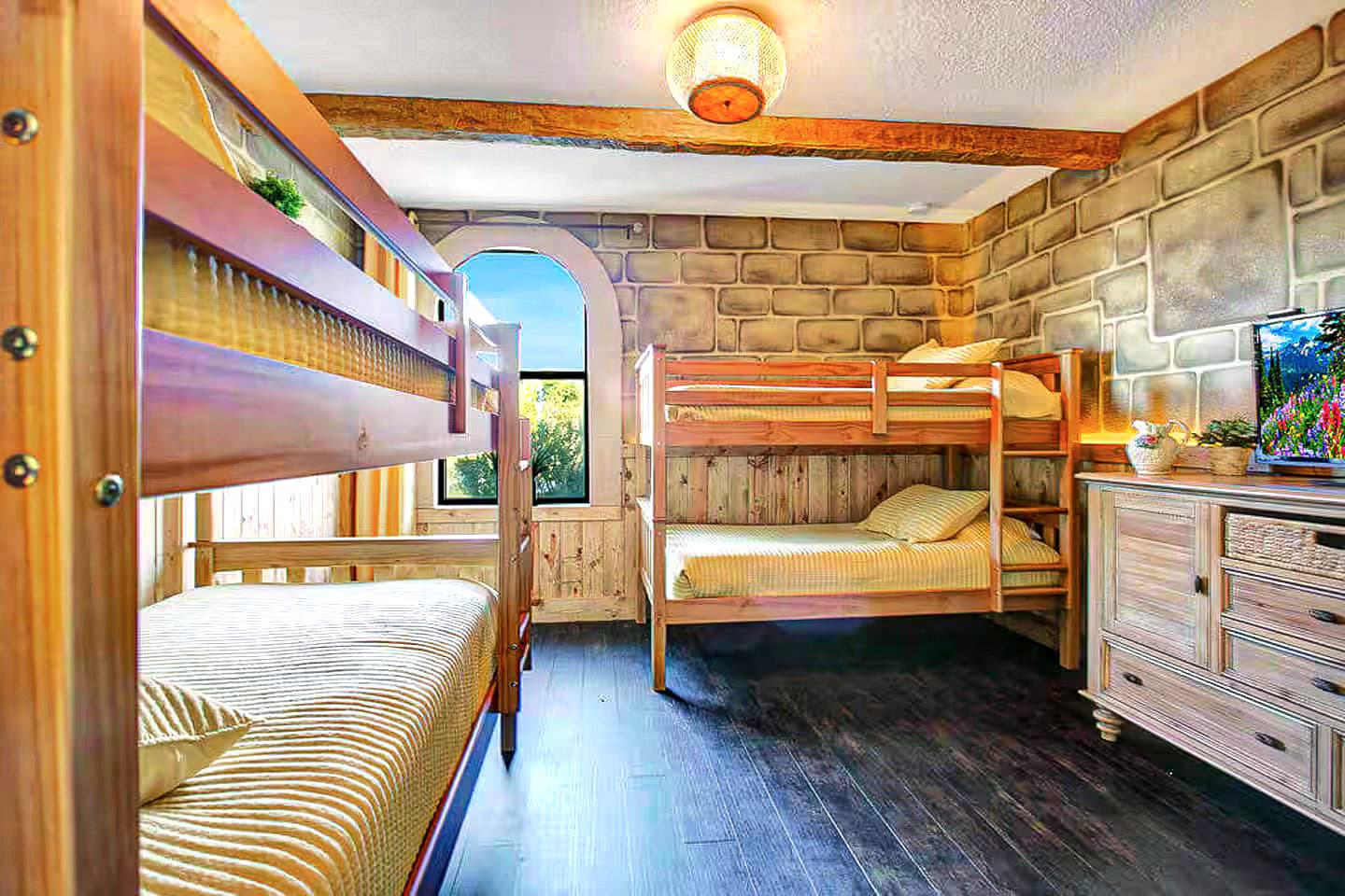 Two sets of sturdy wooden bunks facing each other across honeyed stone walls, go