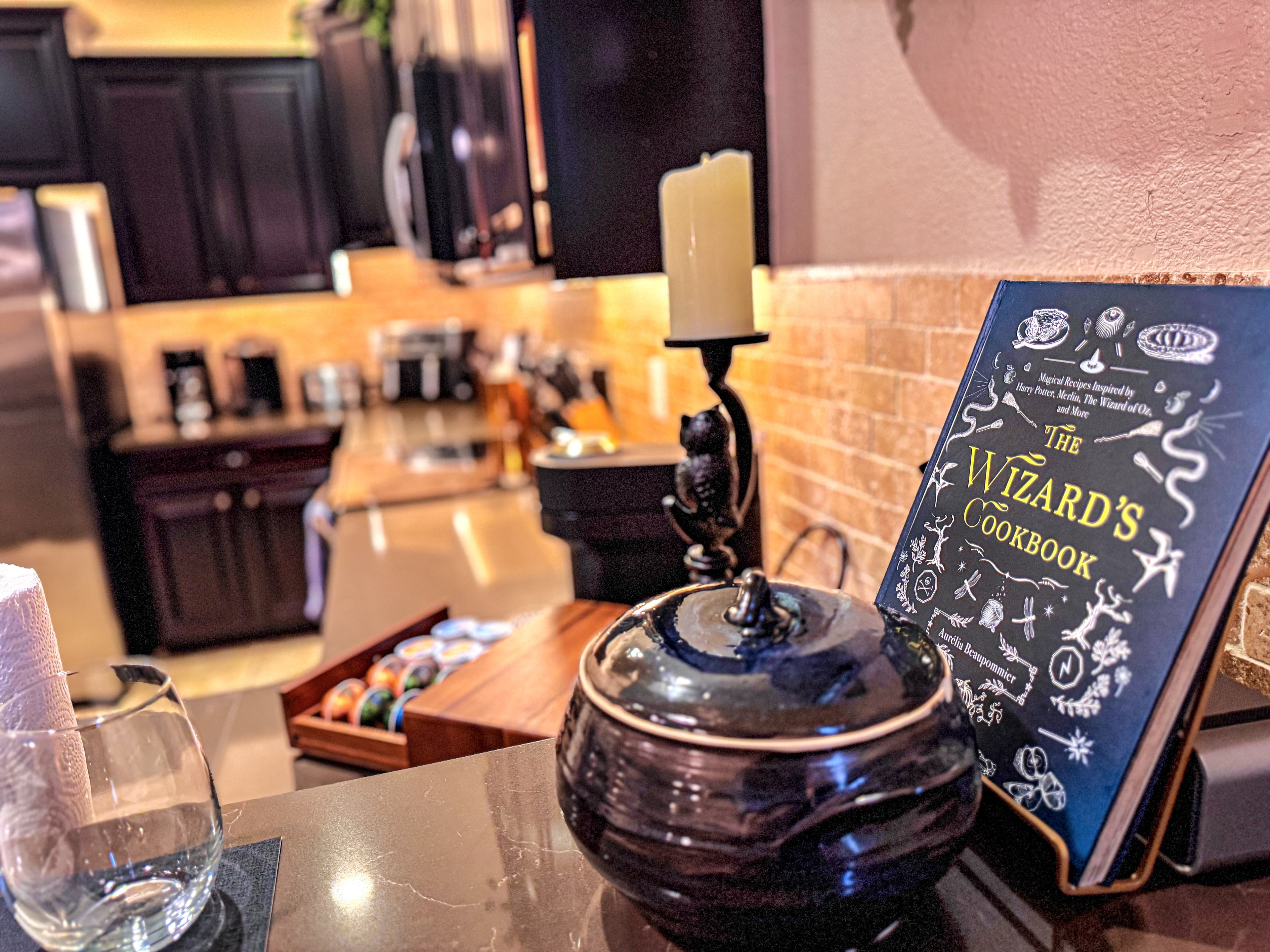 A cast-iron owl guards the counter beside The Wizard’s Cookbook. Behind curved g