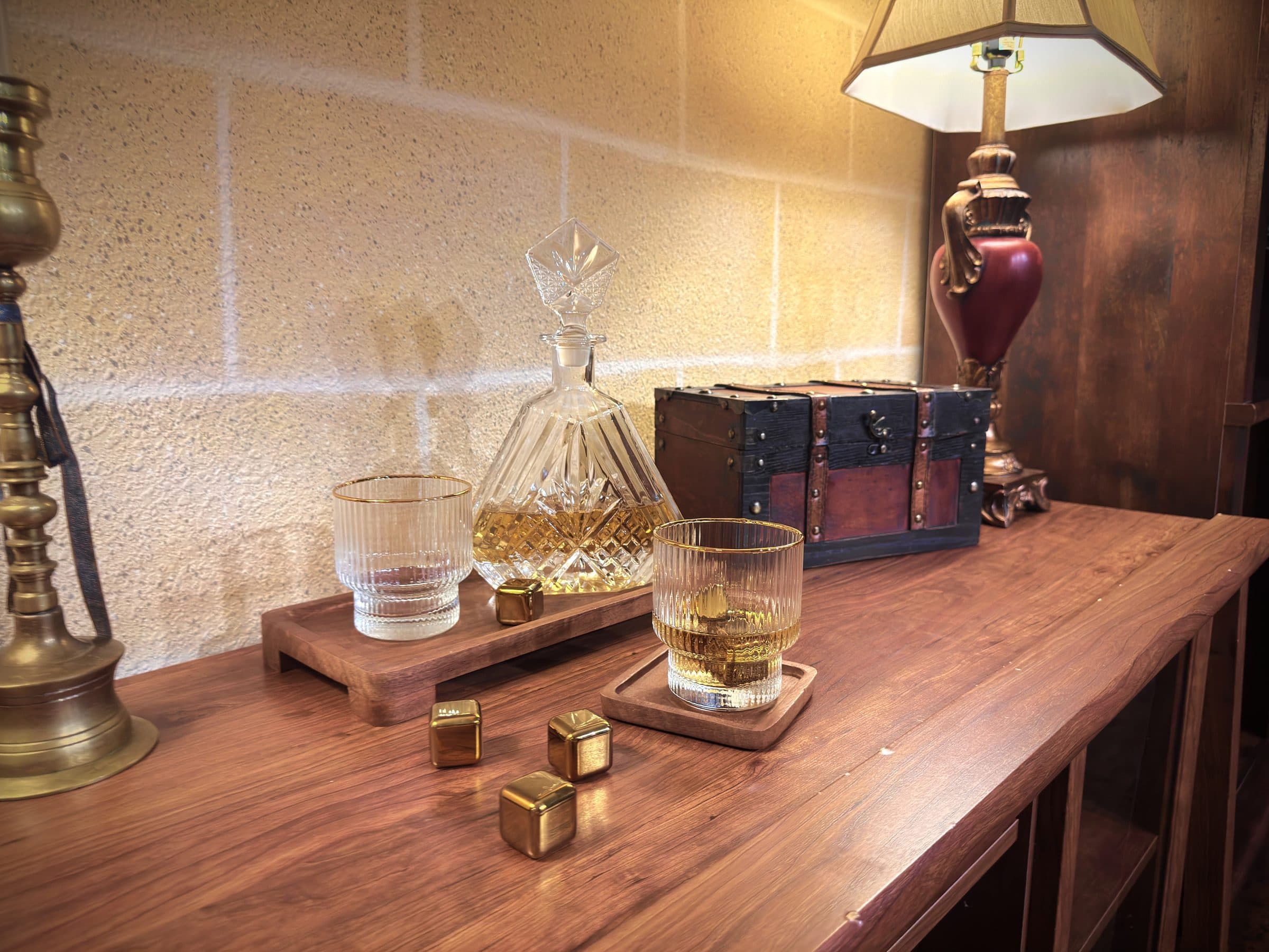 Crystal decanter, cut-glass tumblers, gold whiskey stones on a walnut bar top ag
