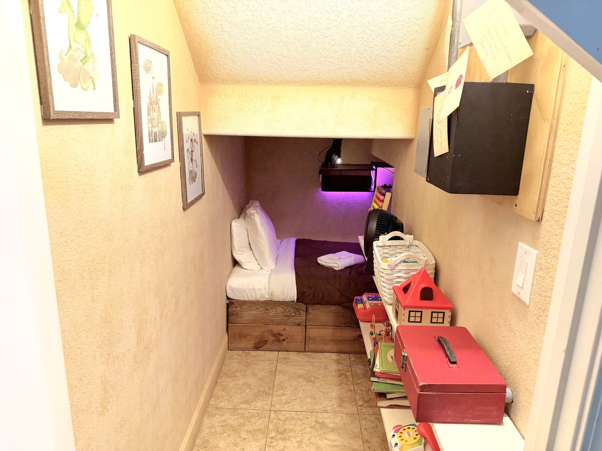 Purple light spilling over the pillow, framed illustrations on the wall, and a c