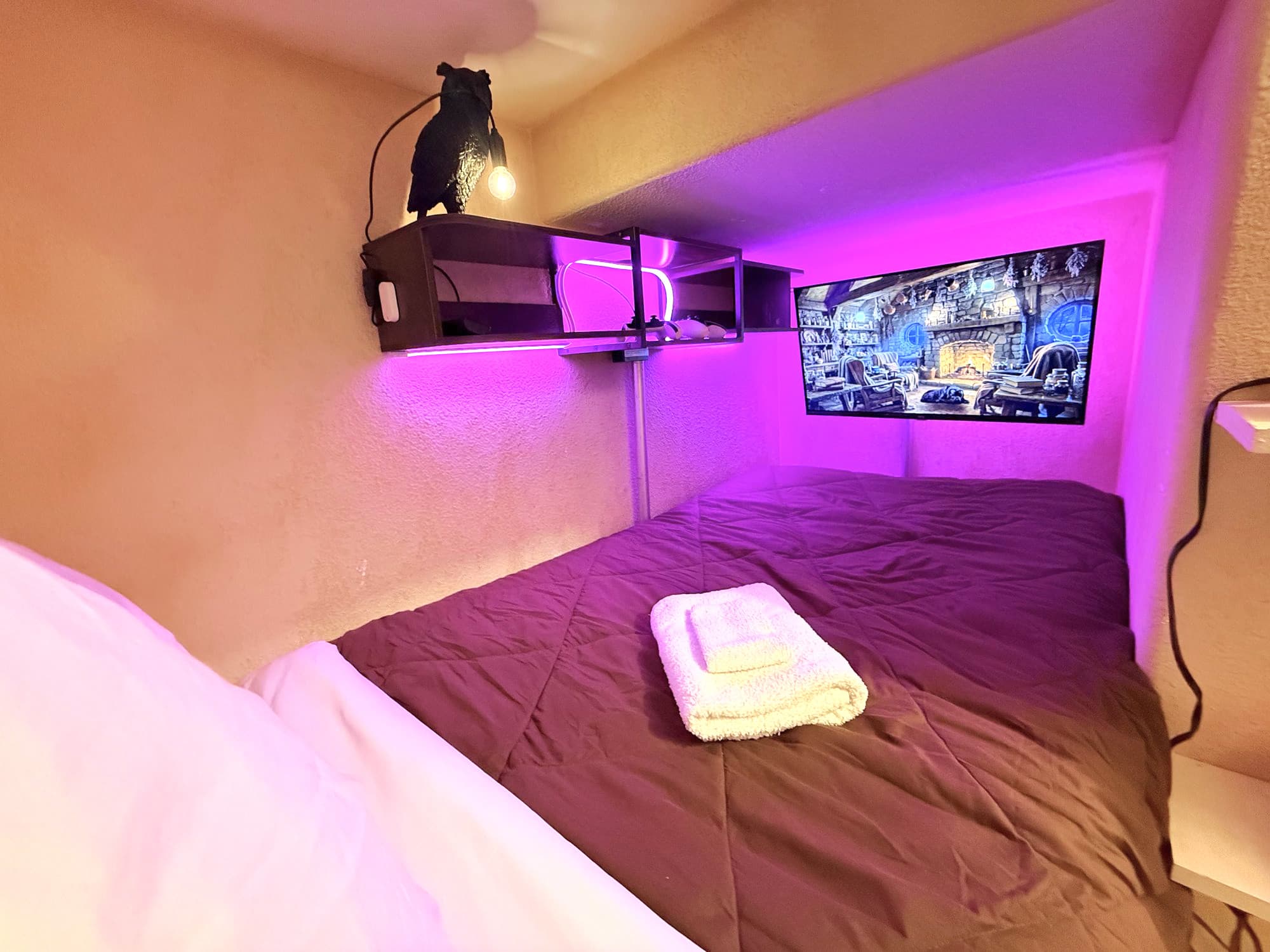 Purple glow washing over dark bedding, an owl lamp standing guard, a TV playing